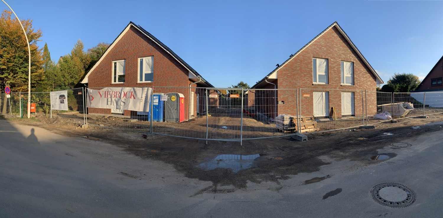 Panoramaansicht von zwei im Bau befindlichen Klinker-Wohnhäusern hinter einem Bauzaun.
