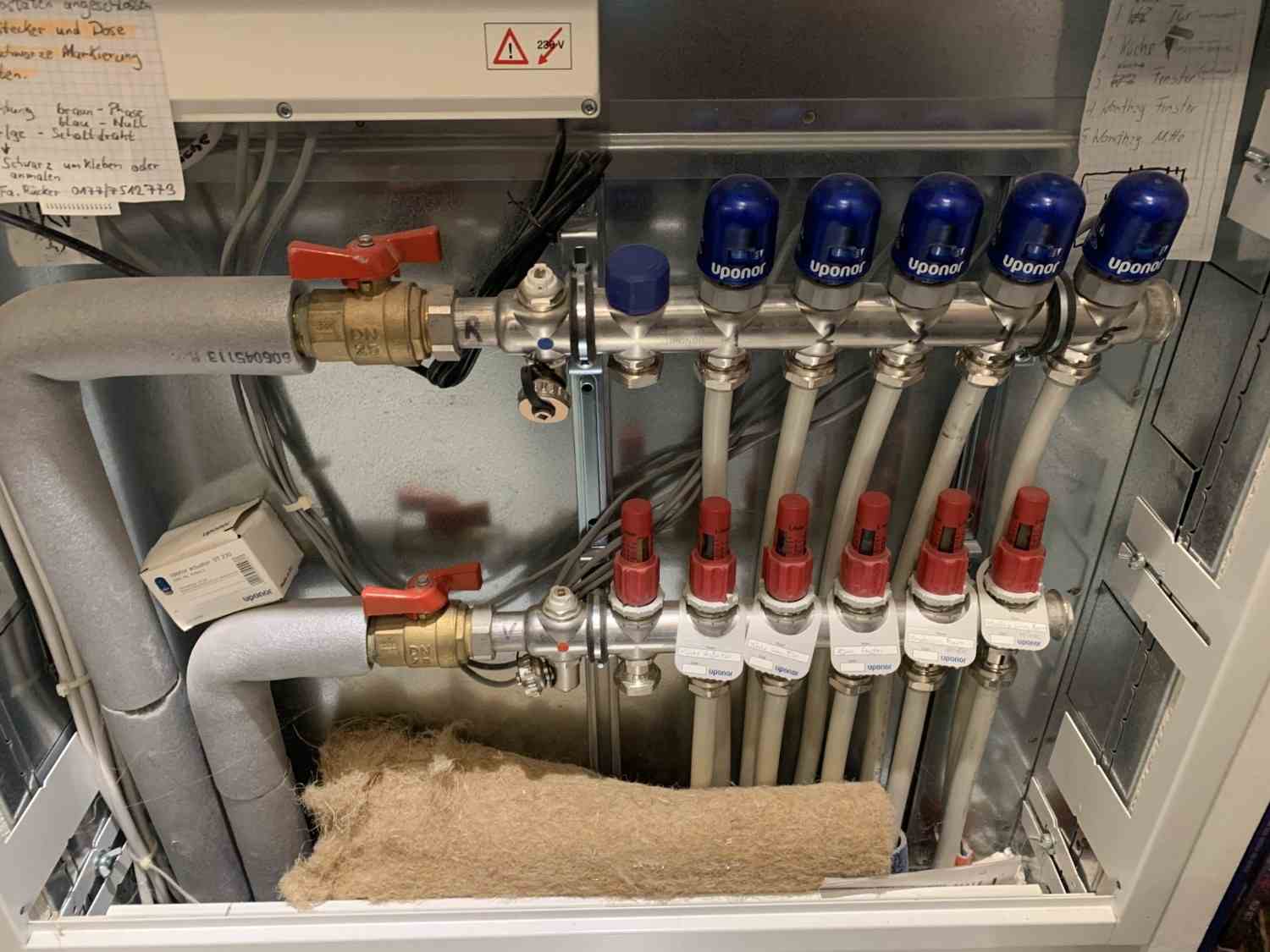 Heizkreisverteiler einer Fußbodenheizung mit Anschlüssen, Stellantrieben und Absperrhähnen im Verteilerkasten.